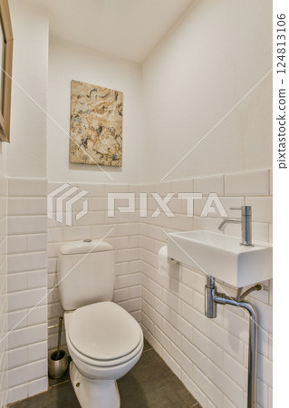 Sleek and minimalistic modern bathroom featuring a white toilet, sink, and stylish wall art complemented by elegant tiles and natural light. Sleek and minimalistic modern bathroom featuring a white toilet, sink, and stylish wall art complemented by elegant tiles and natural light. 124813106
