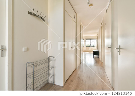 A spacious and modern hallway featuring minimalist decor, light-colored walls, and wooden flooring, complemented by natural light from large windows. 124813140