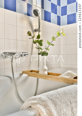 A tranquil bathroom showcasing a minimalist design with blue tiles, a wooden shelf, a soft towel, and a touch of greenery for a relaxing ambiance. 124813197
