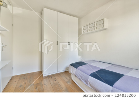 A bright and minimalist bedroom featuring a white wardrobe against a light wall and a checkered bedspread, emphasizing simplicity and calm. A bright and minimalist bedroom featuring a white wardrobe against a light wall and a checkered bedspread, emphasizing simplicity and calm. 124813200