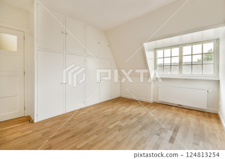 A spacious and minimalist interior featuring clean white walls, a wardrobe, and ample natural light from a large window, perfect for modern living. 124813254