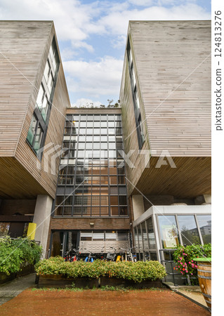 A contemporary building featuring a wooden exterior and large glass windows, surrounded by greenery, showcasing modern architectural trends. A contemporary building featuring a wooden exterior and large glass windows, surrounded by greenery, showcasing modern architectural trends. 124813276