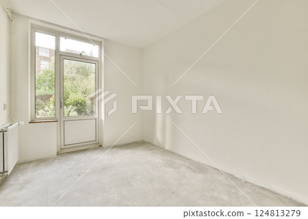 A spacious, empty room featuring a large window that invites natural light in, highlighting the clean and minimalist interior space. 124813279