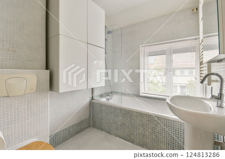 A stylish modern bathroom featuring a sleek soaking tub, contemporary fixtures, and neutral-colored tiles lending a serene ambiance. 124813286