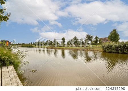 A tranquil view of a calm water body surrounded by lush greenery and a clear sky, showcasing the beauty of nature in a peaceful setting. 124813298