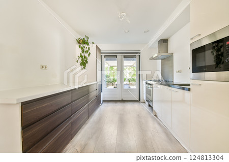 A bright and modern kitchen featuring a minimalist design, sleek cabinets, and large windows that invite natural light into the space. 124813304