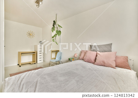 A cozy minimalist bedroom featuring soft pastel colors, a large bed with pink cushions, and contemporary furnishings, creating a calm and inviting atmosphere. 124813342