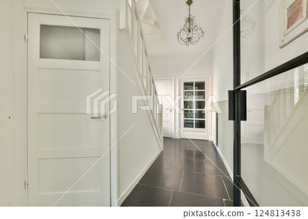 A sleek, modern interior hallway featuring a stylish chandelier, elegant flooring, and well-lit passageway that enhances the home's aesthetic appeal. 124813438