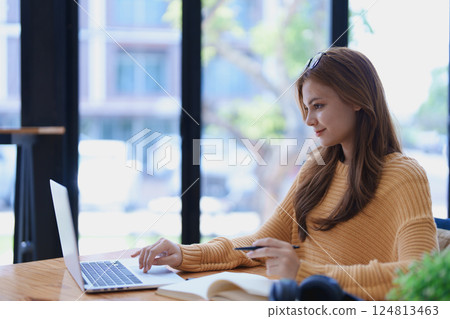 Smiling young woman engaged in online e-learning at her desk with a laptop notebook and headphones creating a positive study atmosphere for success Smiling young woman engaged in online e-learning at her desk with a laptop notebook and headphones creating a positive study atmosphere for success 124813463