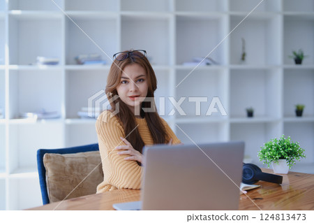 Smiling young woman engaged in online e-learning at her desk with a laptop notebook and headphones creating a positive study atmosphere for success Smiling young woman engaged in online e-learning at her desk with a laptop notebook and headphones creating a positive study atmosphere for success 124813473