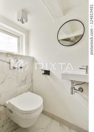 A sleek bathroom featuring elegant marble walls and a contemporary toilet and sink design, illuminated by natural light and stylish fixtures. 124813481