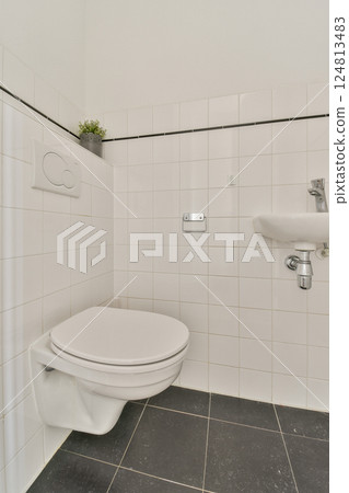 A clean and modern bathroom featuring a white toilet, sleek faucet, and tiled walls, emphasizing minimalist design principles and functionality. 124813483