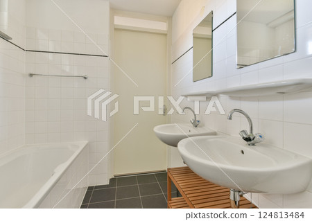 A sleek modern bathroom featuring white tiled walls, double sinks, and wooden accents, creating a stylish and functional space for everyday use. A sleek modern bathroom featuring white tiled walls, double sinks, and wooden accents, creating a stylish and functional space for everyday use. 124813484