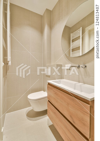 A sleek and contemporary bathroom featuring neutral tones, wooden cabinetry, and functional design elements for efficient use of space. 124813487