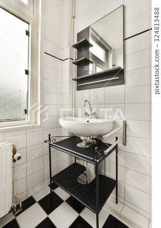 A stylish bathroom featuring a sleek sink, modern mirror, and functional shelving. The space is adorned with black and white tiles, enhancing its contemporary design. 124813488