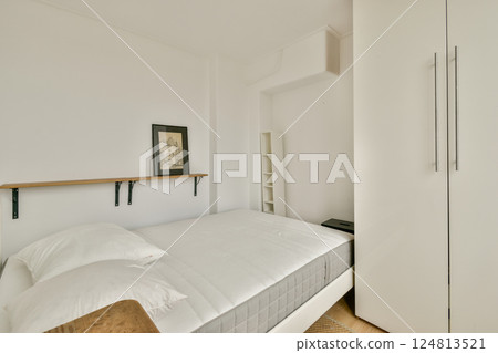 A simple and modern bedroom featuring a bed with white linens, a shelf, and clean lines that create a serene atmosphere. 124813521