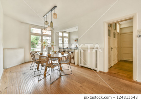 A stylish dining area featuring a wooden table surrounded by elegant chairs and natural light flooding through large windows, enhancing the minimalist aesthetic. 124813548