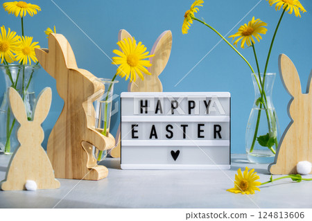 Phrase HAPPY EASTER traditional greeting to christian holiday. Festive mood composition with bunnies and yellow flowers on pastel blue background. Sustainable 124813606