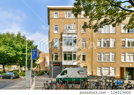 A contemporary building features large windows and balconies, surrounded by trees and parked bicycles, measuring urban lifestyle and green living. A contemporary building features large windows and balconies, surrounded by trees and parked bicycles, measuring urban lifestyle and green living. 124813608