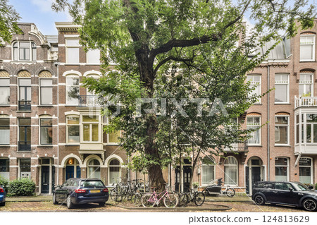 Elegant row of historic buildings framed by trees, showcasing unique architectural styles and urban life in Amsterdam. 124813629