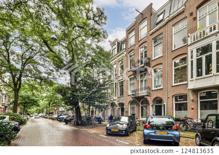 A picturesque street lined with historic brick buildings and lush trees, showcasing the vibrant atmosphere of Amsterdam's canals and local life. A picturesque street lined with historic brick buildings and lush trees, showcasing the vibrant atmosphere of Amsterdam's canals and local life. 124813635