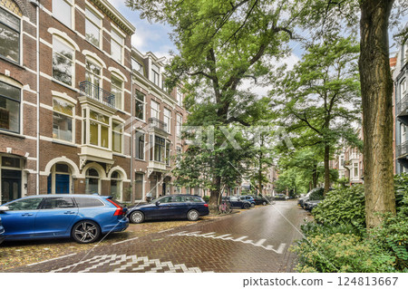 A picturesque view of an Amsterdam street lined with beautiful historic buildings and lush green trees, creating a serene urban atmosphere. A picturesque view of an Amsterdam street lined with beautiful historic buildings and lush green trees, creating a serene urban atmosphere. 124813667