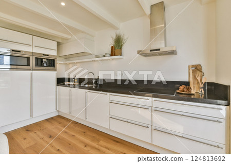 Sleek and modern kitchen featuring white cabinetry, stainless steel appliances, and warm wooden flooring. A perfect blend of functionality and style. 124813692