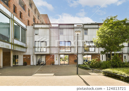 Contemporary building design featuring a mix of materials, with an inviting courtyard and greenery, showcasing urban living and architectural innovation. Contemporary building design featuring a mix of materials, with an inviting courtyard and greenery, showcasing urban living and architectural innovation. 124813721