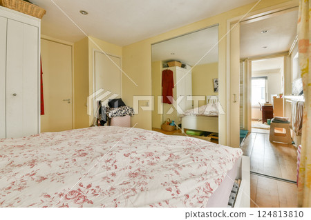 A bright and inviting bedroom showcasing a floral-patterned bedspread, minimalist furniture, and warm tones, perfect for relaxation and comfort. 124813810
