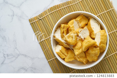 Close-up of deep-fried tofu in a white bowl on a bamboo mat on a white marble table. Flat-lay food image with space. Close-up of deep-fried tofu in a white bowl on a bamboo mat on a white marble table. Flat-lay food image with space. 124813883