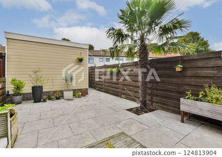 An inviting outdoor garden area features modern stone paving, lush greenery, and a wooden fence creating a peaceful retreat at home. 124813904