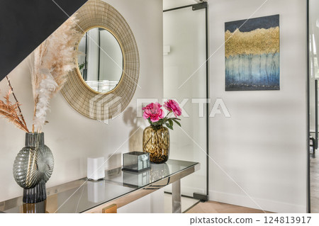 A stylish modern interior featuring a decorative mirror, floral arrangements, and contemporary artwork that enhances the overall ambiance of the space. A stylish modern interior featuring a decorative mirror, floral arrangements, and contemporary artwork that enhances the overall ambiance of the space. 124813917