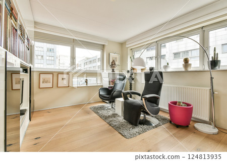 A stylish office interior featuring a sleek black chair, wall art, and natural light streaming through large windows, creating a productive atmosphere. 124813935