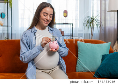 Pregnant woman inserting banknote money cash dollar in piggybank saving for baby's future needs 124813946