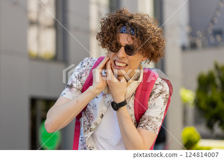 Man tourist suffering from toothache feels pain holds his hand near his cheek on city street 124814007