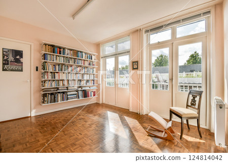 A spacious reading room featuring a modern bookshelf filled with books, a wooden chair, and large windows allowing natural light to illuminate the space. A spacious reading room featuring a modern bookshelf filled with books, a wooden chair, and large windows allowing natural light to illuminate the space. 124814042