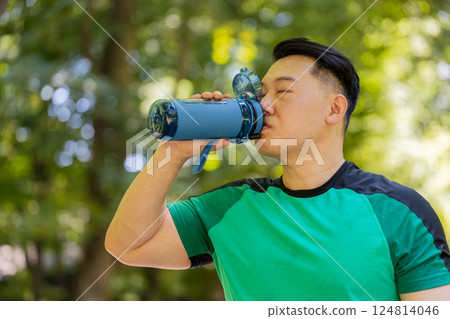Sporty athletic thirsty Chinese Asian sportsman runner jogger drinking water after workout in park Sporty athletic thirsty Chinese Asian sportsman runner jogger drinking water after workout in park 124814046