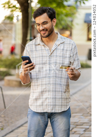 Indian young man using credit card smartphone while transferring money, purchases online outdoors Indian young man using credit card smartphone while transferring money, purchases online outdoors 124814052