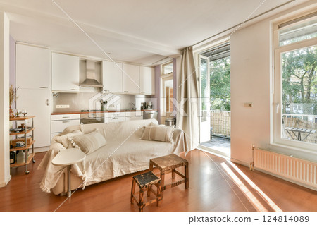 A stylish and open kitchen design featuring light tones, wooden flooring, and windows that allow natural light, creating a welcoming space. 124814089
