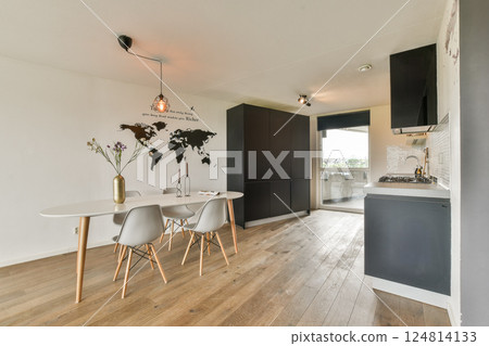 This interior showcases a sleek, modern kitchen with a dining area, featuring stylish furniture and a minimalist decor with wooden flooring. 124814133
