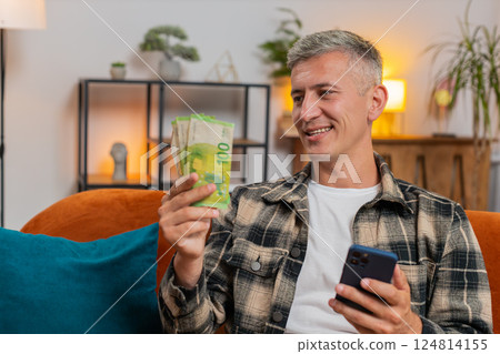 Smiling happy Caucasian man counting money euro cash use smartphone income salary lottery game win 124814155
