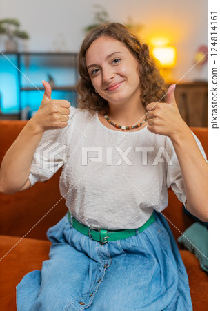 Portrait of excited smiling Caucasian woman showing double thumbs up sitting on sofa couch at home Portrait of excited smiling Caucasian woman showing double thumbs up sitting on sofa couch at home 124814161