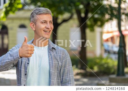 Happy mature man showing thumbs up agrees giving positive reply recommends good idea on city street 124814168