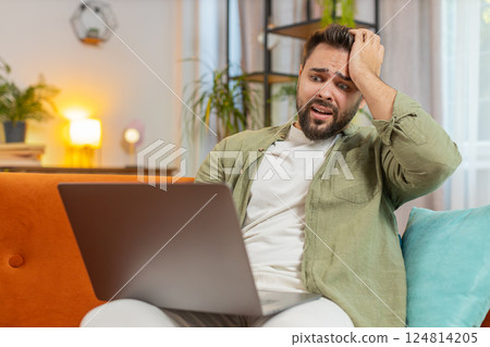 Upset young Caucasian young man sitting on sofa at home using laptop having anxiety and stress Upset young Caucasian young man sitting on sofa at home using laptop having anxiety and stress 124814205