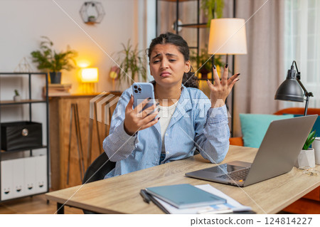 Upset displeased woman freelancer using smartphone reading bad news sitting at home office table 124814227