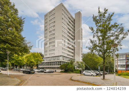 A striking modern building towers over a landscaped urban area, reflecting contemporary design amidst greenery and roads, showcasing a blend of nature and architecture. 124814239
