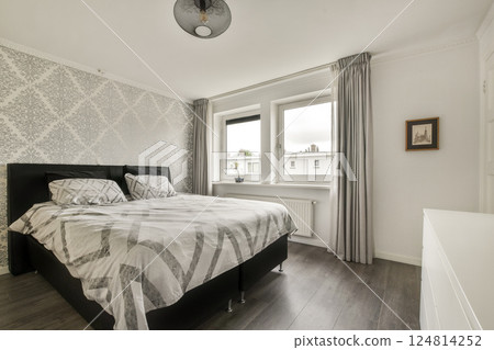 A bright and stylish bedroom featuring patterned wallpaper, large windows, and modern furnishings, creating a serene and inviting atmosphere. 124814252