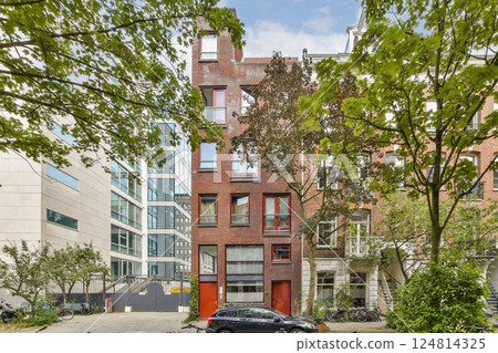 A vibrant modern building stands amidst lush trees and other structures, exemplifying contemporary urban design and integrating nature with city life. 124814325