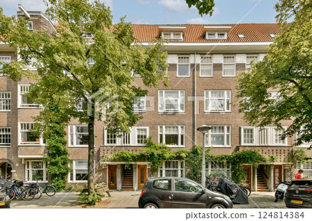 A picturesque view of a charming urban residential building enveloped by vibrant green trees, showcasing a beautiful blend of nature and architecture. A picturesque view of a charming urban residential building enveloped by vibrant green trees, showcasing a beautiful blend of nature and architecture. 124814384