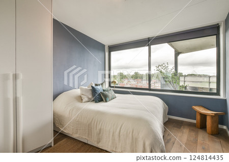 A stylish and airy bedroom featuring a minimalist design, large windows offering a panoramic view, and elegant decor elements adding to the tranquil atmosphere. A stylish and airy bedroom featuring a minimalist design, large windows offering a panoramic view, and elegant decor elements adding to the tranquil atmosphere. 124814435